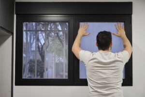 Young latin man installing frosted window vinyl on wet window glass.